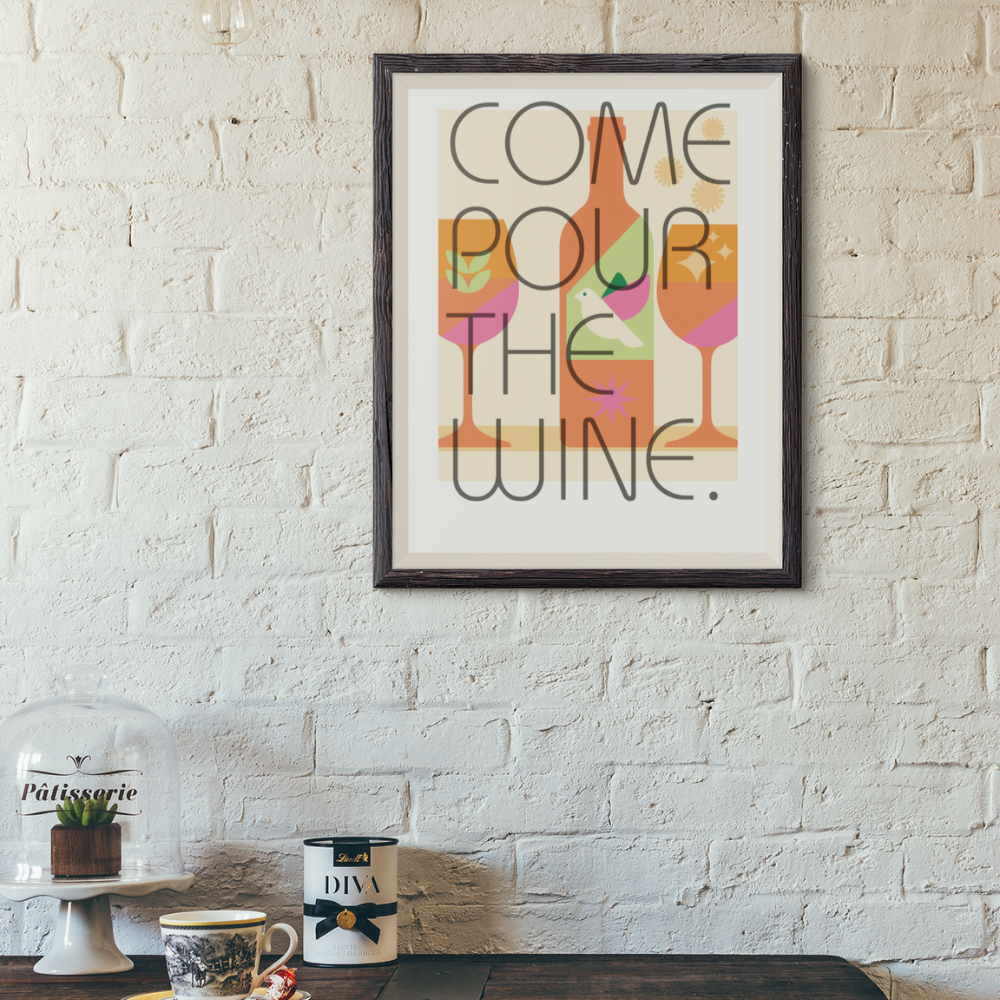 Framed poster with 'Pour the Wine' text on a brick wall above a wooden table.