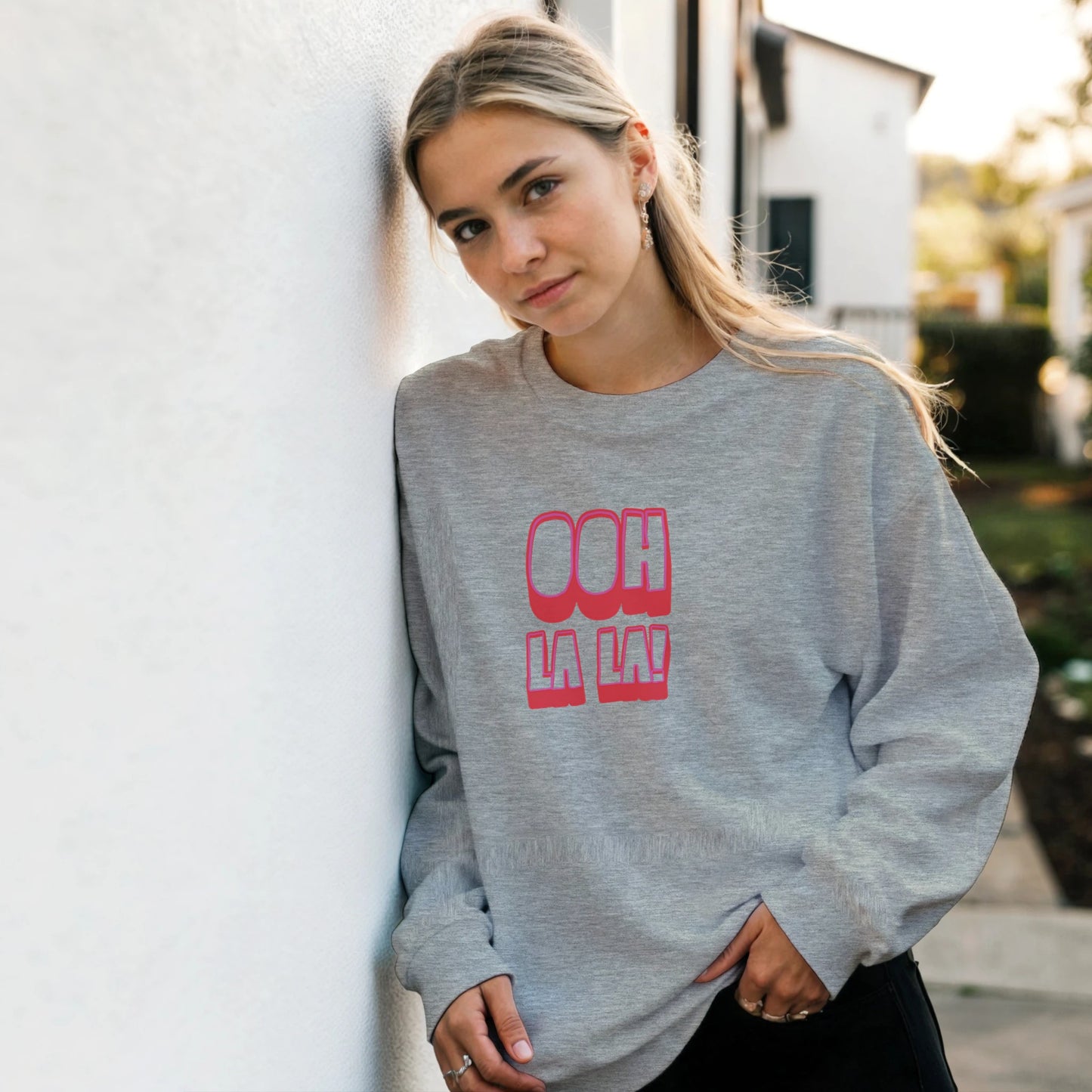 Woman wearing grey Ooh La La sweatshirt by Taste Union, relaxed fit unisex jumper with pink retro lettering, casual outdoor lifestyle photo