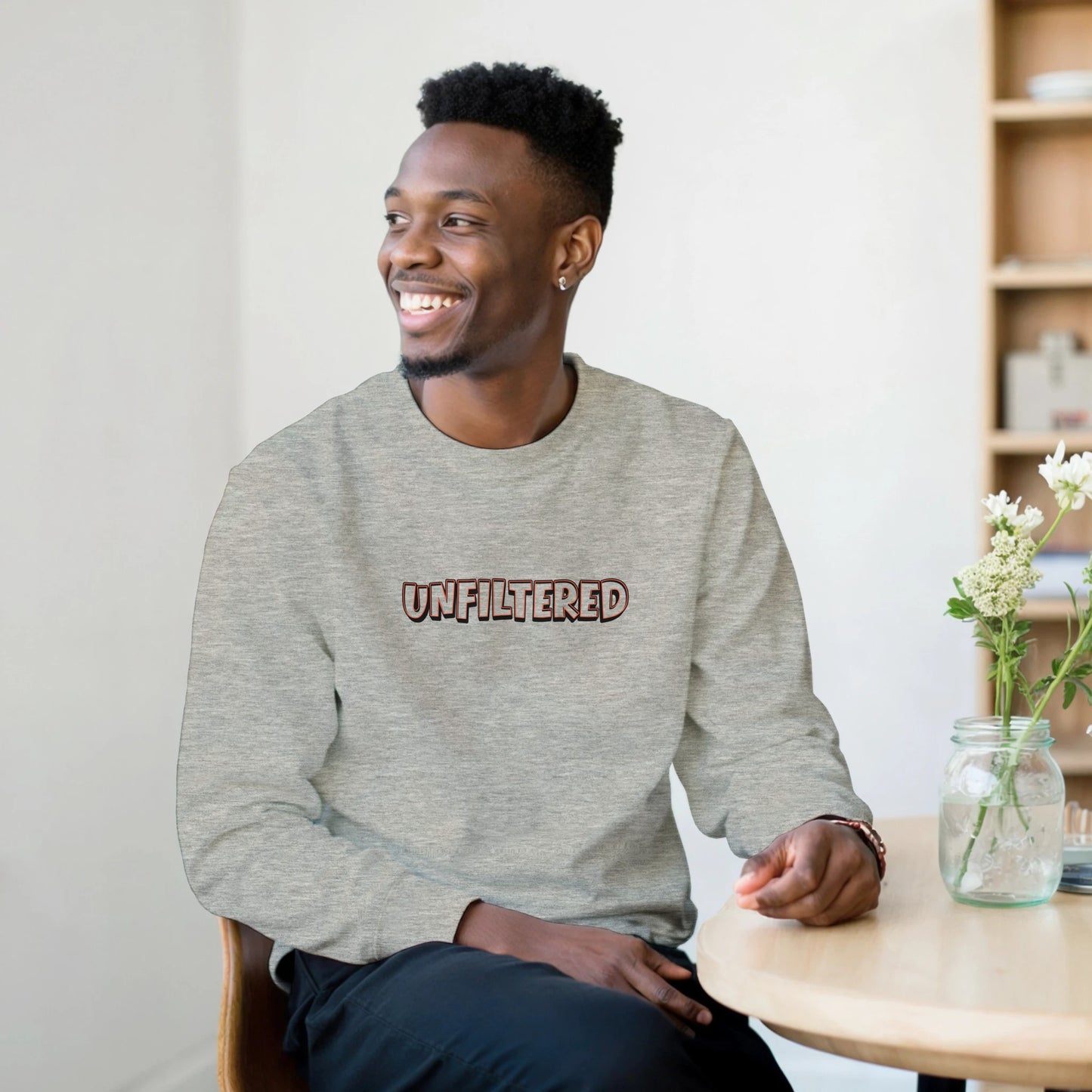 Model wearing Unfiltered sweatshirt by Taste Union — unisex grey crewneck with brown text design inspired by natural wine and authenticity, photographed in a relaxed indoor café setting.