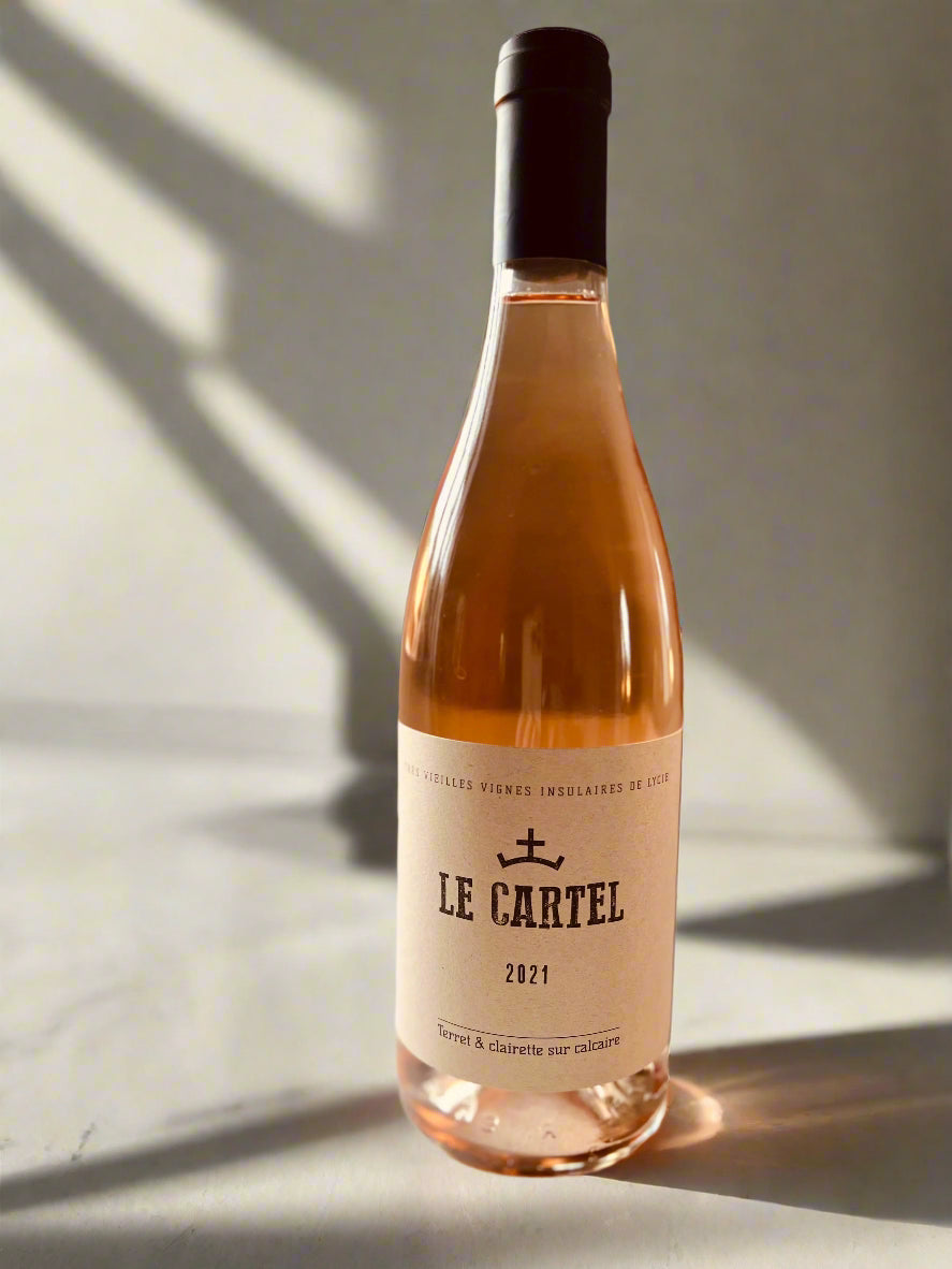 A bottle of Le Cartel Rosé 2021 wine on a light surface, showcasing its elegant label and golden-pink hue. Organic Grenache Noir from Gruissan Plage.