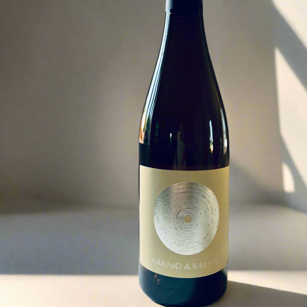 Bottle of Sarrat de Goundy Mano o Mano Blanc 2021 white wine with a minimalist circular label design, photographed on a light background.