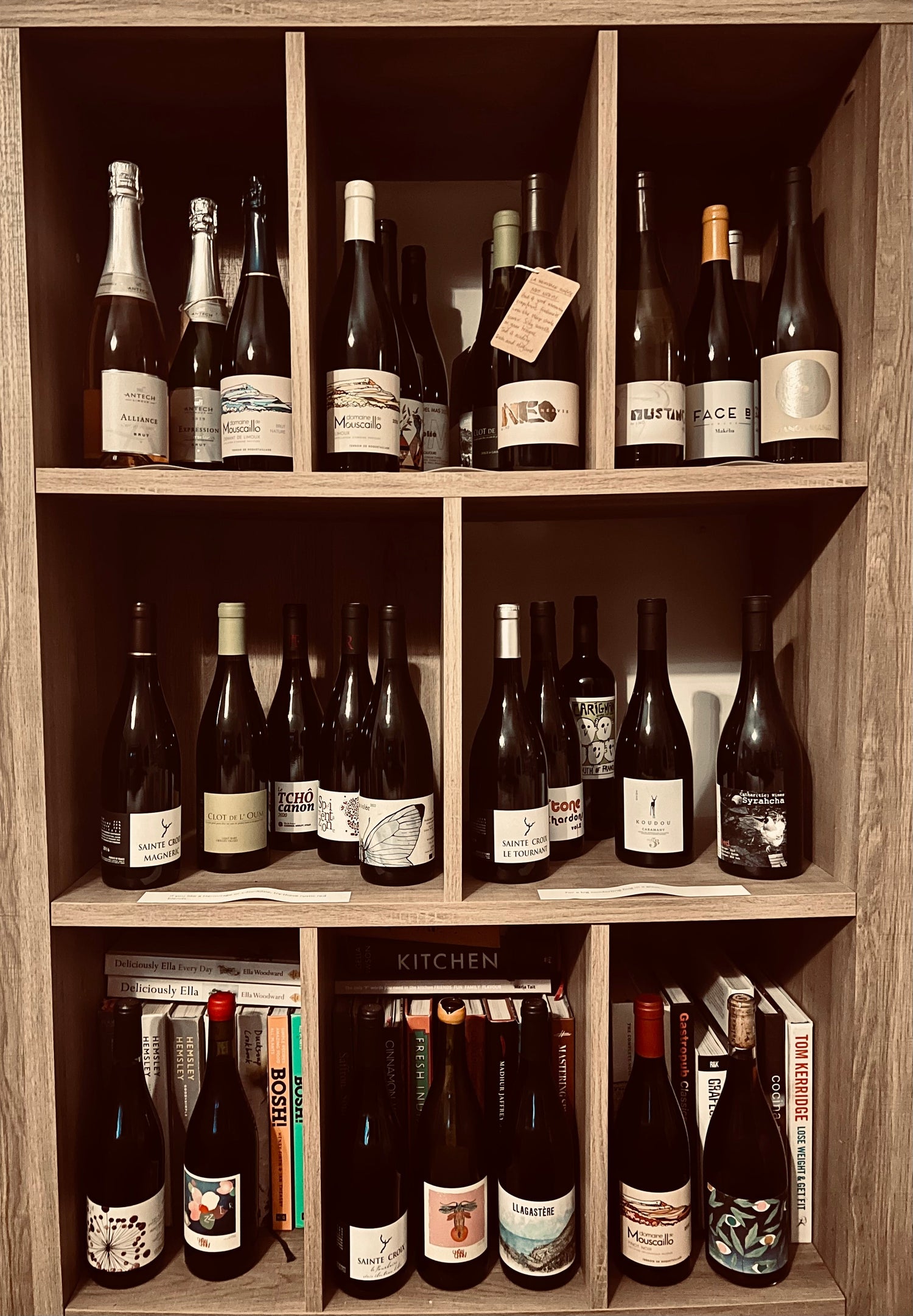 This image showcases a well-curated collection of wine bottles organized in a wooden shelving unit. The collection appears to focus on artisanal and natural wines, with an emphasis on unique labels and diverse regions.