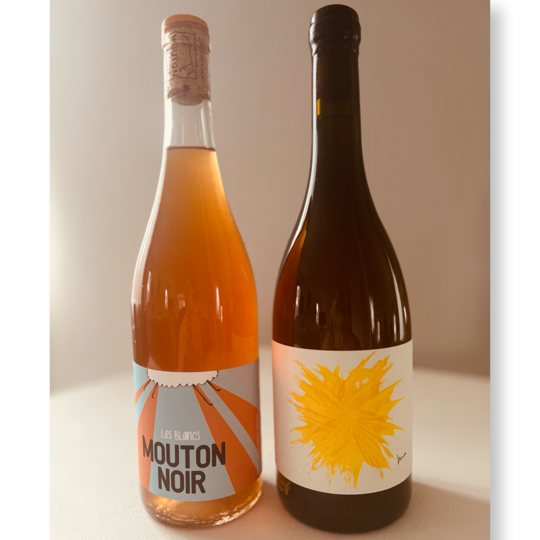 Two bottles of orange wine - Mouton Noir 'Les Blancs' on the left with a bright label design, and Gilles Troullier Orange Wine from Roussillon on the right with a distinctive yellow abstract label.