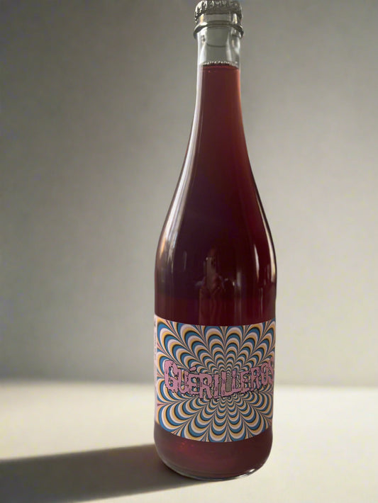 A bottle of Gilles Troullier Guerrilleros 2022 light red wine, featuring a colourful label with a hypnotic spiral design. The bottle is photographed on a light surface with a soft focus background.