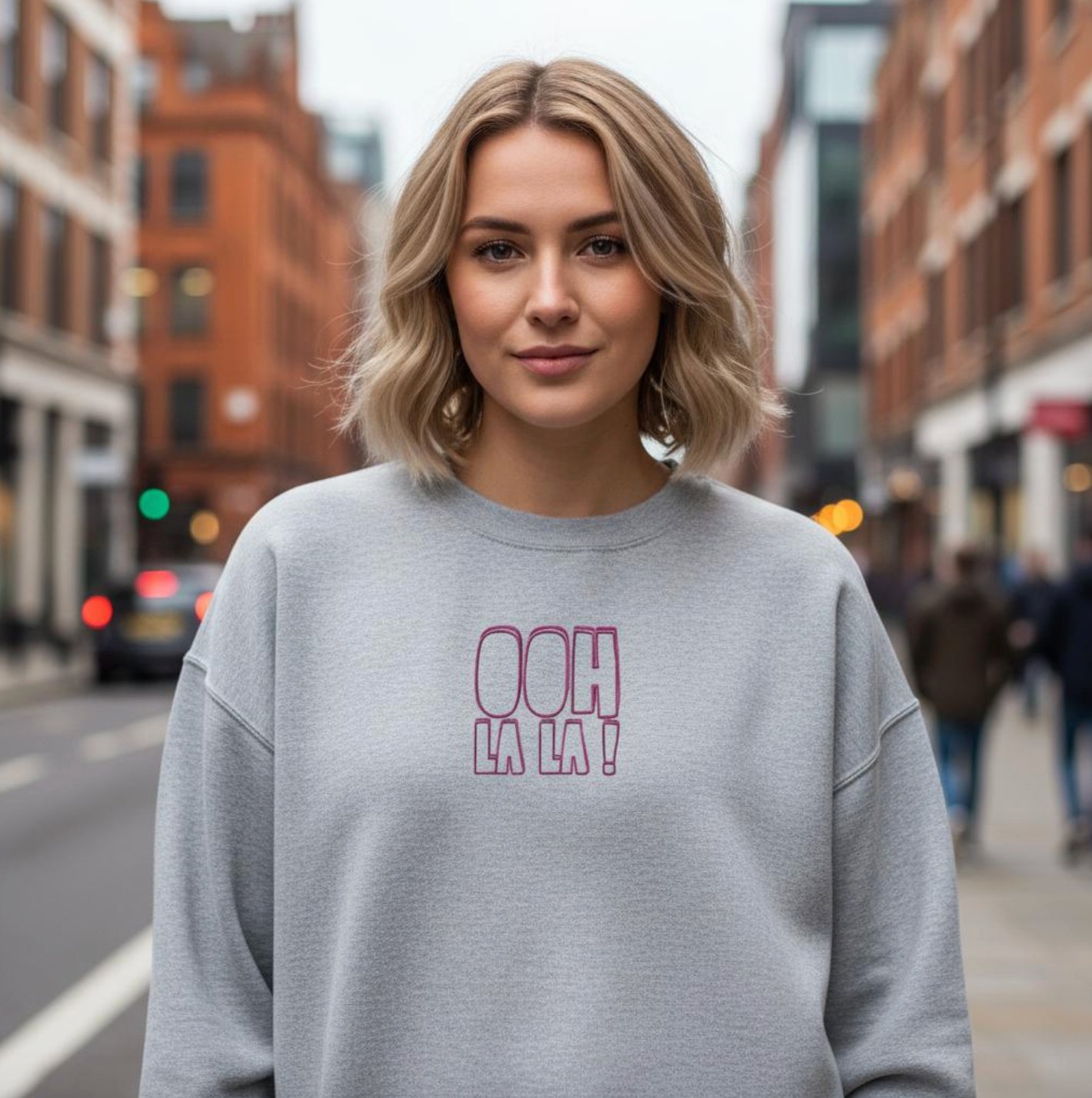 Woman wearing a gray sweatshirt with 'Ooh La La!' text on a city street.