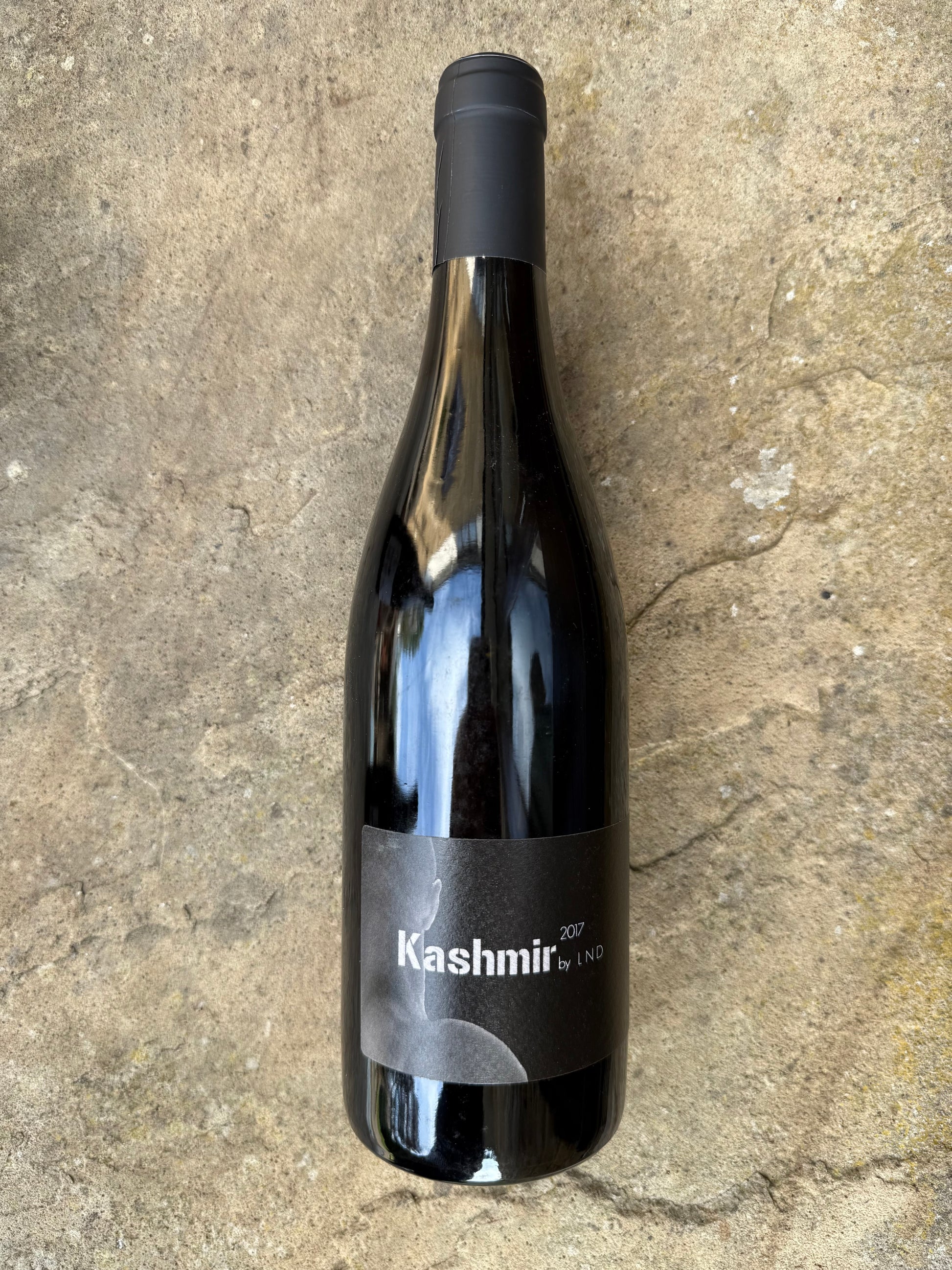 Bottle of Kashmir 2017 by La Nouvelle Don(n)e, a natural red wine with a bold label, photographed on stone—aged, organic, and perfect for BBQ pairings.