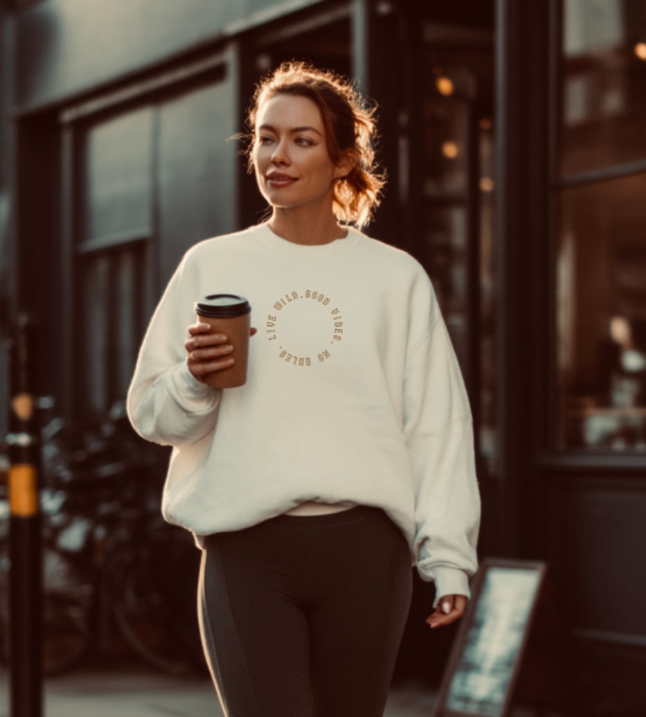Woman wearing a white sweatshirt with a circular design, holding a coffee cup, walking outdoors.