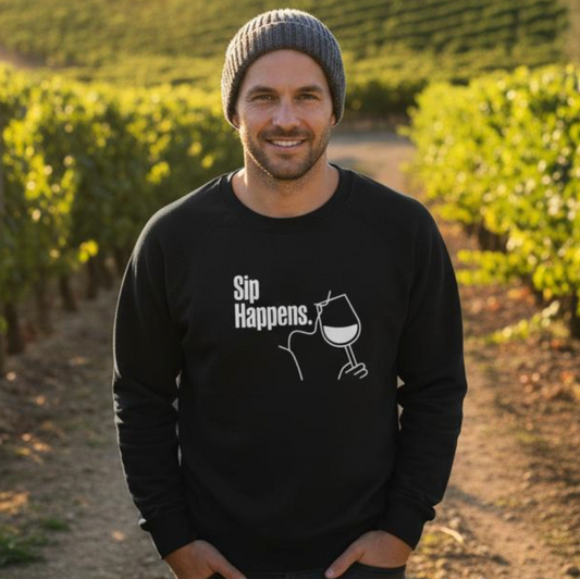 Man wearing a black sweatshirt with 'Sip Happens' text in a vineyard setting