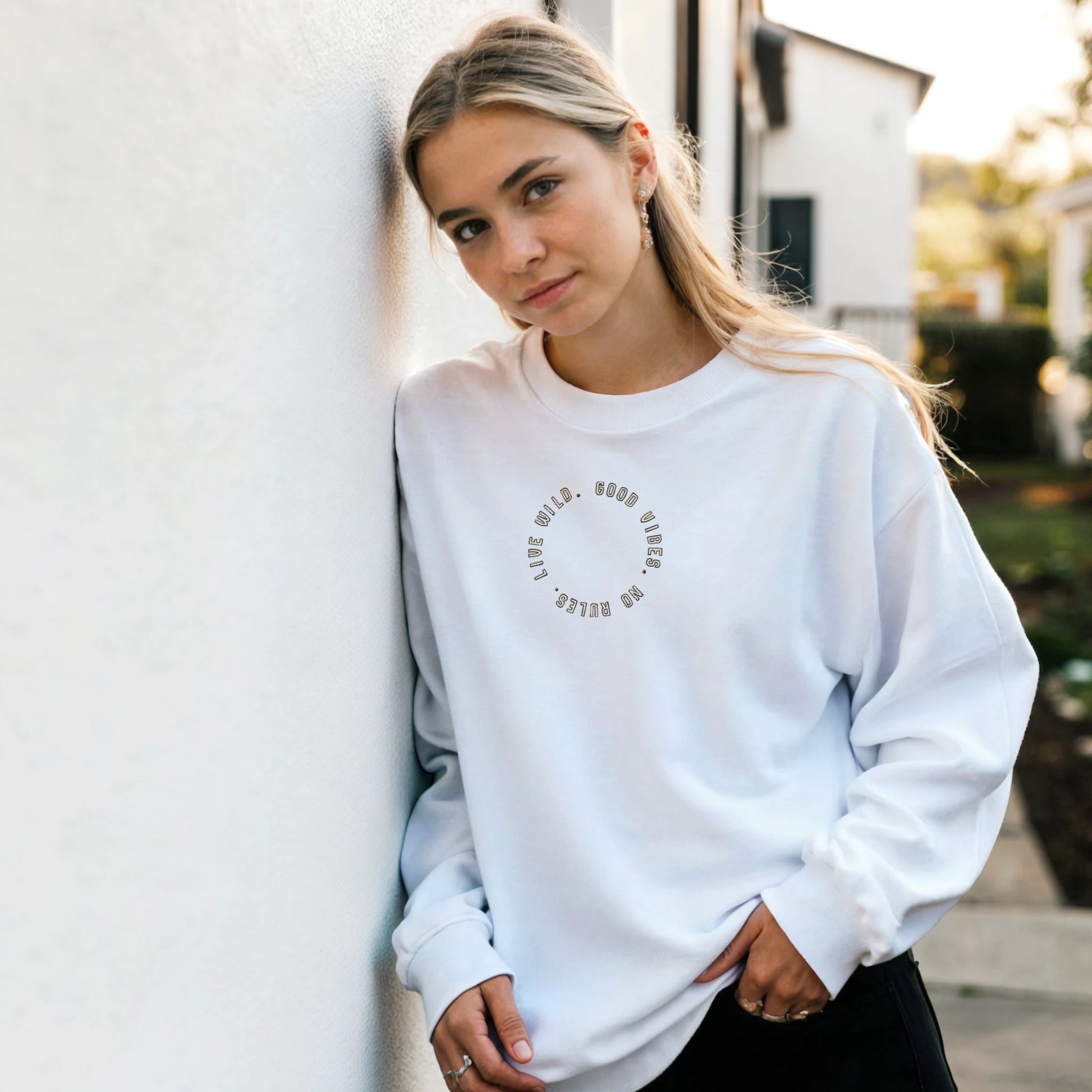 Woman wearing white embroidered sweatshirt with gold stitched text ‘Good Vibes, No Rules, Live Wild’ — unisex sustainable gift by Taste Union.