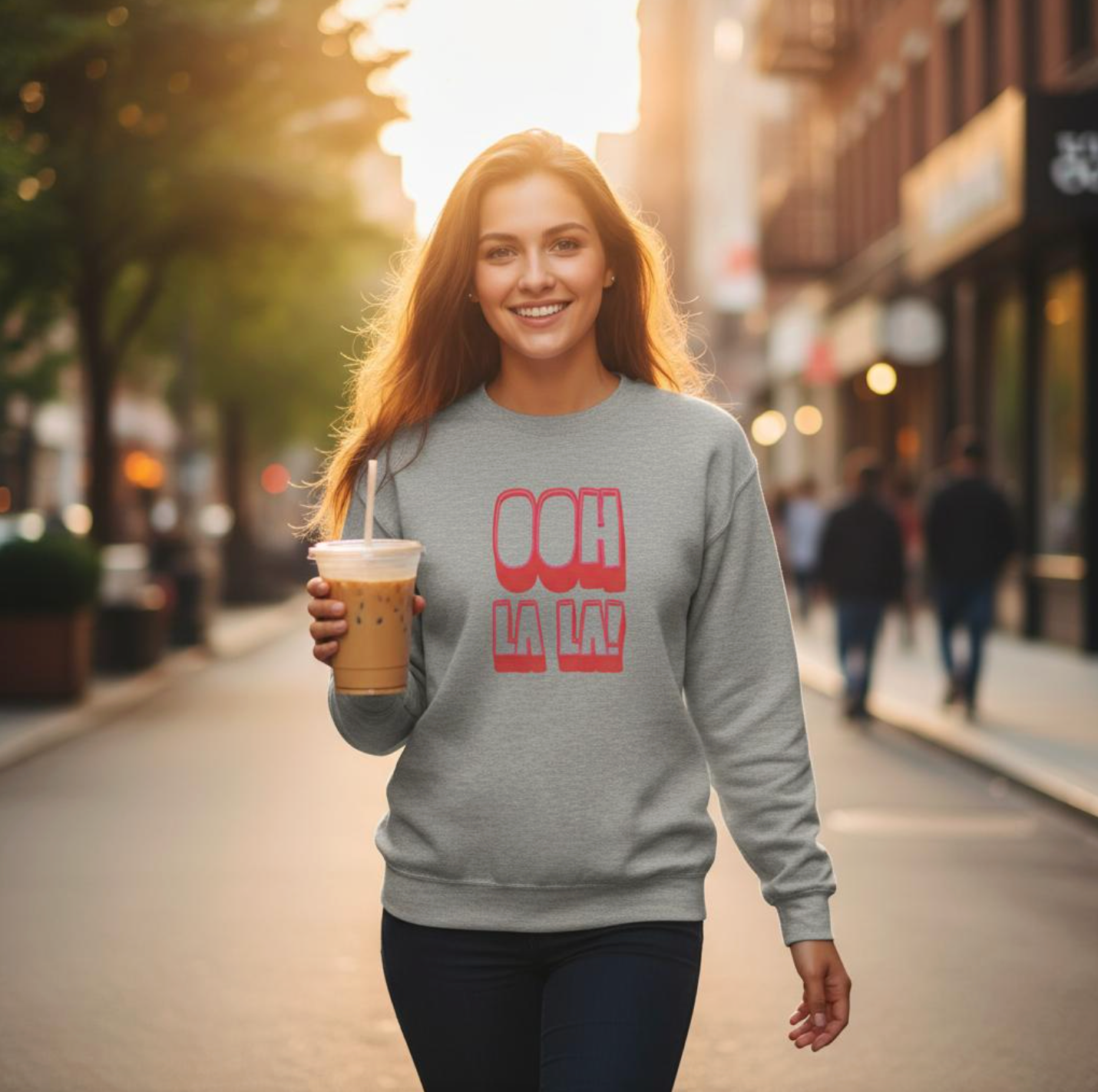 Model wearing the Ooh La La! sweatshirt by Taste Union — unisex grey crewneck with bold red text inspired by French wine culture, photographed in warm evening city light.