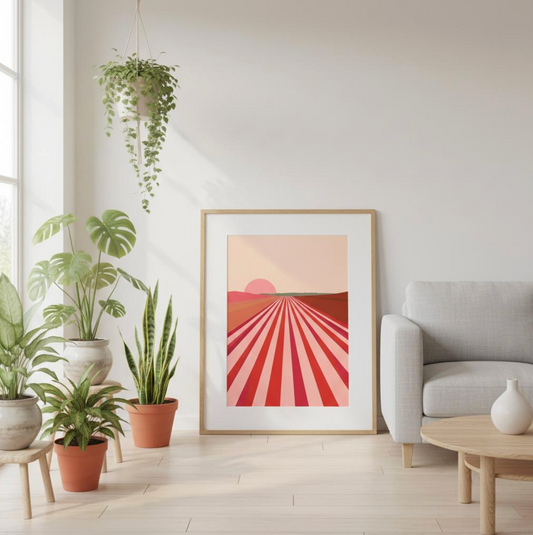 Framed Taste Union pink vineyard art print leaning against a bright white wall surrounded by greenery — soft sunlight and terracotta pots create a peaceful, natural vignette.