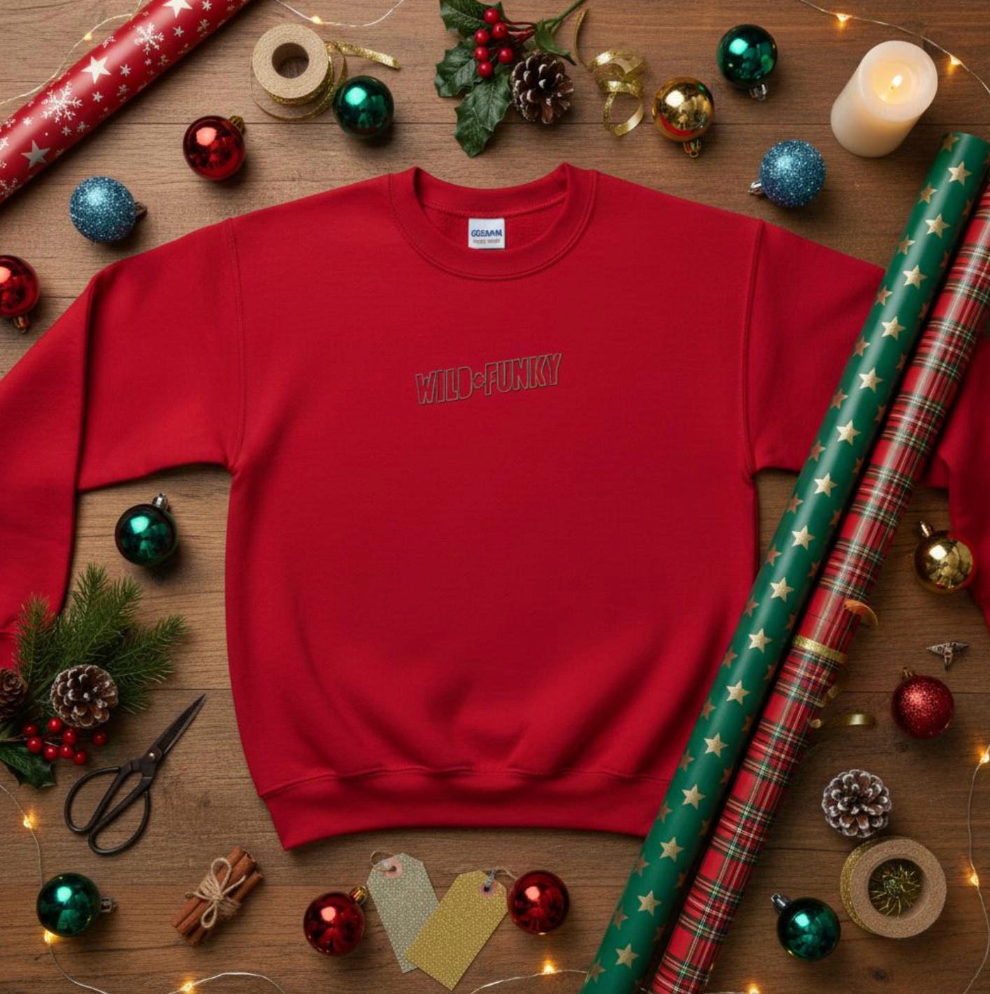 Red ‘Wild + Funky’ embroidered sweatshirt styled in a Christmas flat-lay with wrapping paper, ornaments, candles and festive decorations.