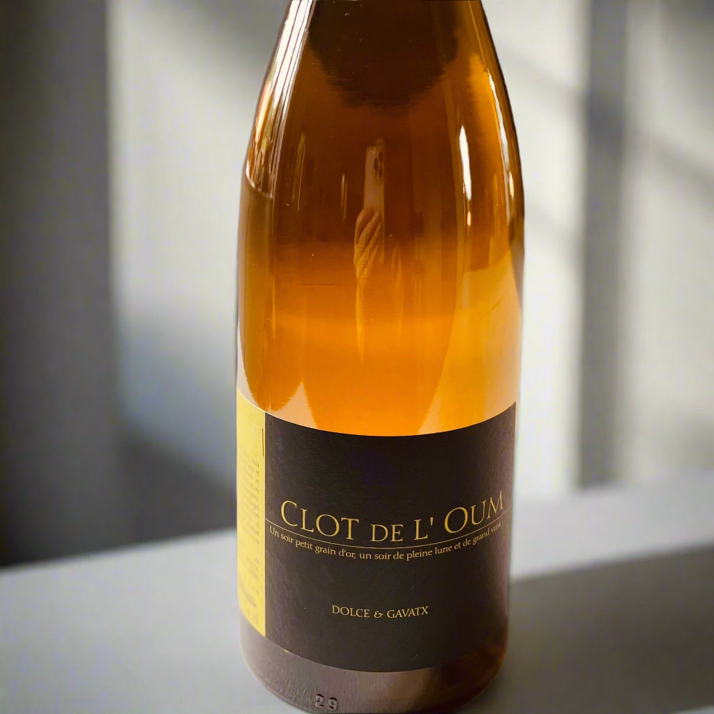 A bottle of Clot de l'Oum Dolce & Gavatx 2019 white wine, featuring a golden-amber hue with a sleek label displaying the winery name and wine details. Perfectly lit against a soft neutral background, highlighting the elegant design and biodynamic craftsmanship of the wine.