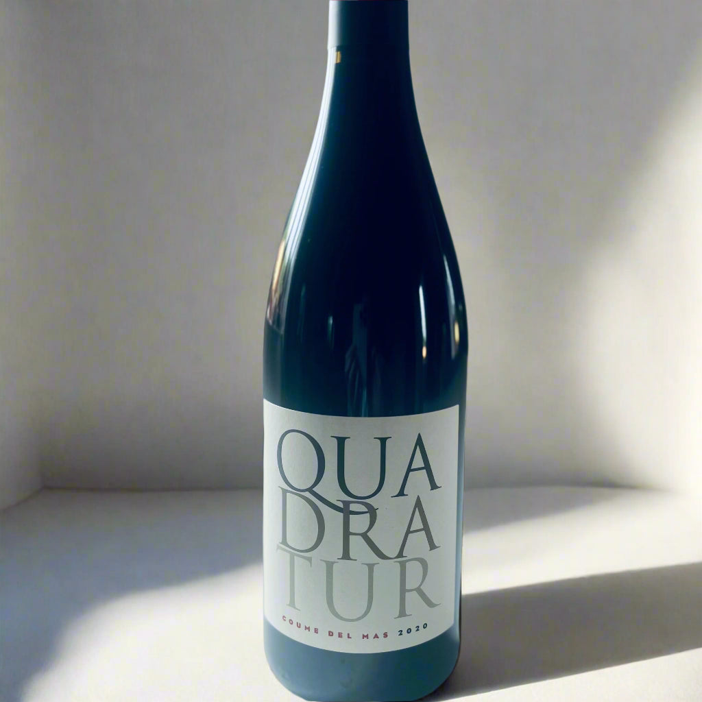 A bottle of Coume del Mas Quadratur 2020 red wine placed on a white surface, with minimalist lighting emphasszing the elegant wine label design.