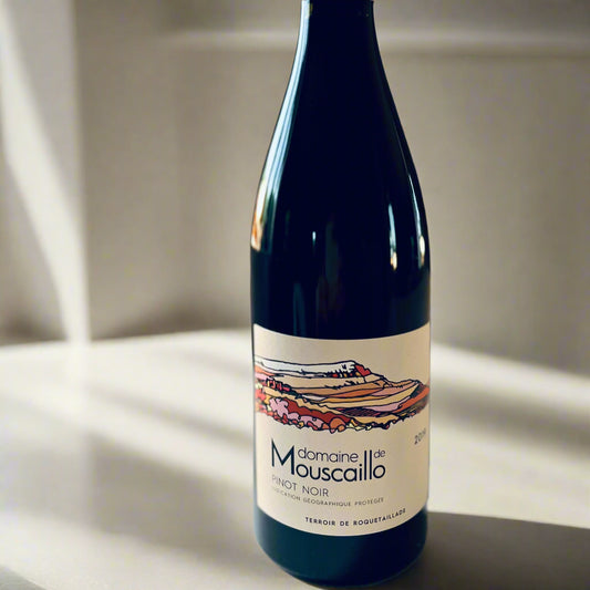 Bottle of Domaine de Mouscaillo Pinot Noir 2019 with label featuring colourful vineyard artwork, placed on a light surface in soft lighting.