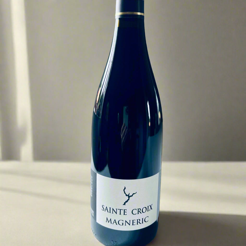 Bottle of Domaine Sainte Croix Magneric 2016 red wine, featuring a minimalist label design with a tree branch icon, placed on a white table.