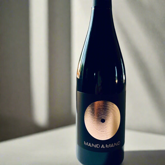 Bottle of Sarrat de Goundy Mano a Mano Rouge 2019, featuring a dark wine bottle with a gold circular emblem, placed on a light surface.

